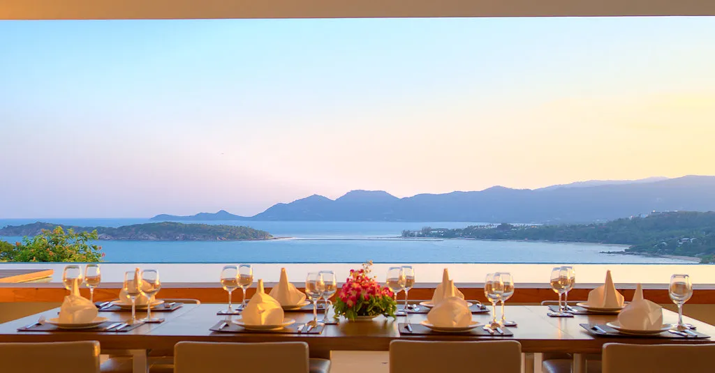 Outdoor dining table set for eight at a luxury villa, looking out over a sweeping panoramic view of the bay in Koh Samui