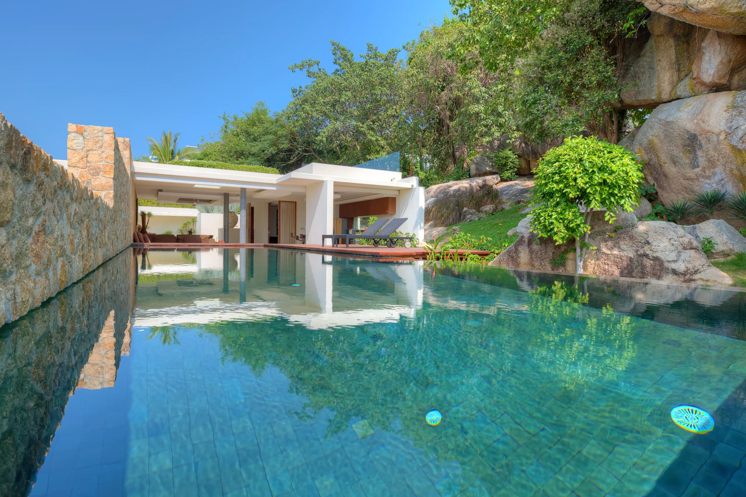 Low-angle view of private pool and villa surrounded by tropical cliffside greenery, Koh Samui